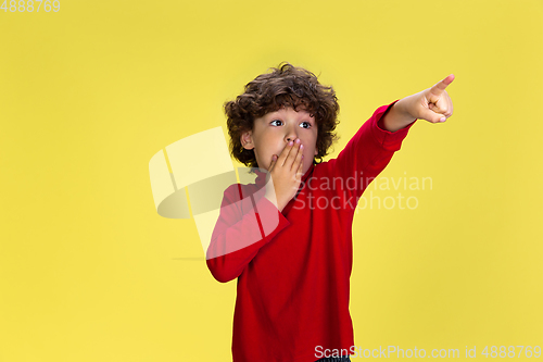 Image of Pretty young curly boy in red wear on yellow studio background. Childhood, expression, fun.