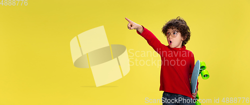 Image of Pretty young curly boy in red wear on yellow studio background. Childhood, expression, fun.