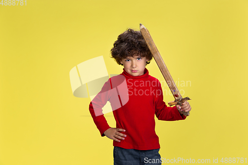 Image of Pretty young curly boy in red wear on yellow studio background. Childhood, expression, fun.