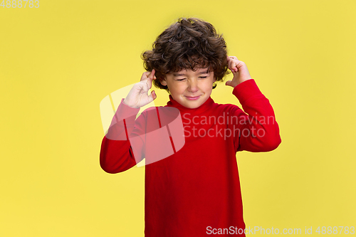 Image of Pretty young curly boy in red wear on yellow studio background. Childhood, expression, fun.