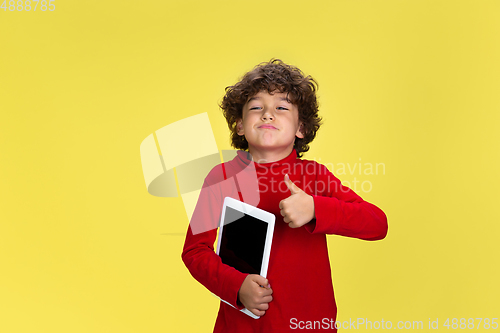 Image of Pretty young curly boy in red wear on yellow studio background. Childhood, expression, fun.