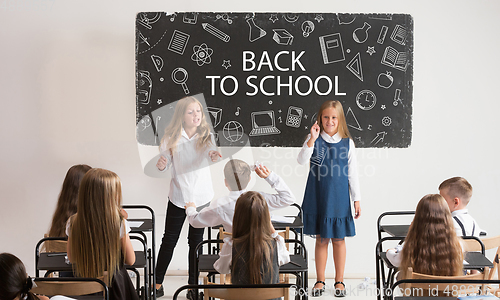 Image of School children in classroom at lesson with worlds Back to school on classboard