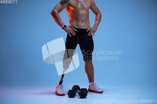 Image of Athlete with disabilities or amputee isolated on blue studio background. Professional male sportsman with leg prosthesis training with weights in neon