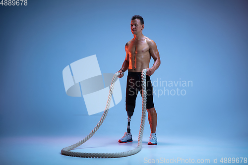 Image of Athlete with disabilities or amputee isolated on blue studio background. Professional male sportsman with leg prosthesis training with weights in neon