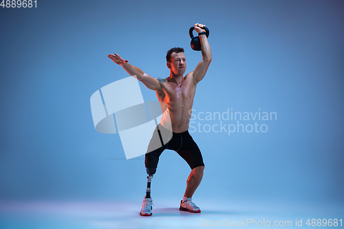 Image of Athlete with disabilities or amputee isolated on blue studio background. Professional male sportsman with leg prosthesis training with weights in neon