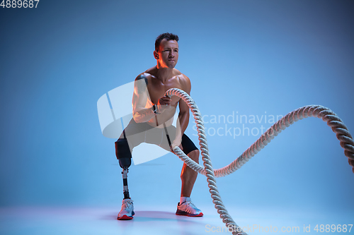 Image of Athlete with disabilities or amputee isolated on blue studio background. Professional male sportsman with leg prosthesis training with weights in neon