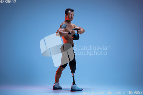 Image of Athlete with disabilities or amputee isolated on blue studio background. Professional male sportsman with leg prosthesis training with weights in neon