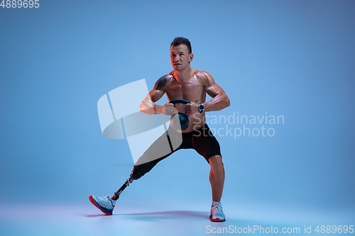 Image of Athlete with disabilities or amputee isolated on blue studio background. Professional male sportsman with leg prosthesis training with weights in neon