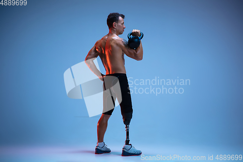 Image of Athlete with disabilities or amputee isolated on blue studio background. Professional male sportsman with leg prosthesis training with weights in neon