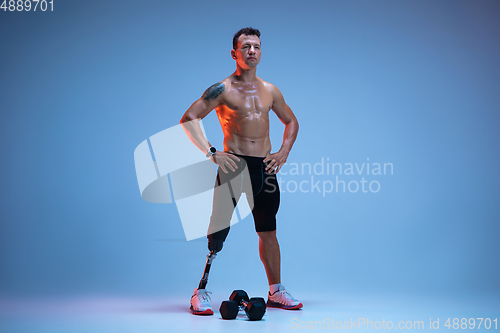Image of Athlete with disabilities or amputee isolated on blue studio background. Professional male sportsman with leg prosthesis training with weights in neon