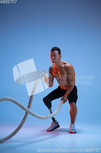 Image of Athlete with disabilities or amputee isolated on blue studio background. Professional male sportsman with leg prosthesis training with weights in neon