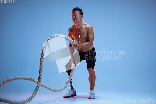 Image of Athlete with disabilities or amputee isolated on blue studio background. Professional male sportsman with leg prosthesis training with weights in neon