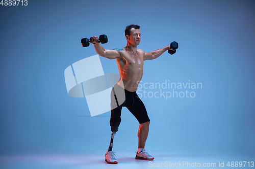 Image of Athlete with disabilities or amputee isolated on blue studio background. Professional male sportsman with leg prosthesis training with weights in neon