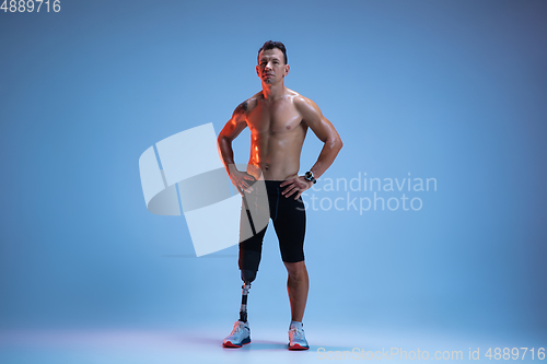 Image of Athlete with disabilities or amputee isolated on blue studio background. Professional male sportsman with leg prosthesis training with weights in neon