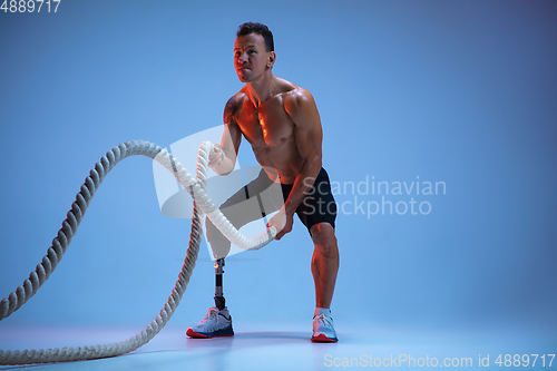 Image of Athlete with disabilities or amputee isolated on blue studio background. Professional male sportsman with leg prosthesis training with weights in neon