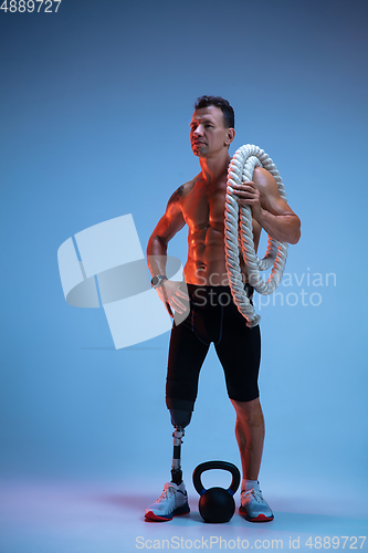 Image of Athlete with disabilities or amputee isolated on blue studio background. Professional male sportsman with leg prosthesis training with weights in neon