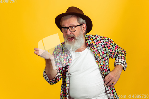 Image of Senior hipster man wearing eyeglasses posing on yellow background. Tech and joyful elderly lifestyle concept