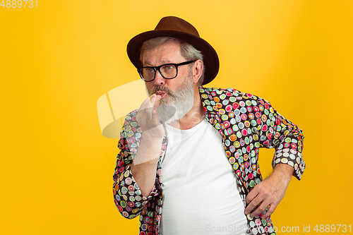 Image of Senior hipster man wearing eyeglasses posing on yellow background. Tech and joyful elderly lifestyle concept