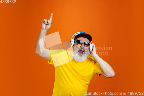 Image of Senior hipster man using devices, gadgets on orange background. Tech and joyful elderly lifestyle concept