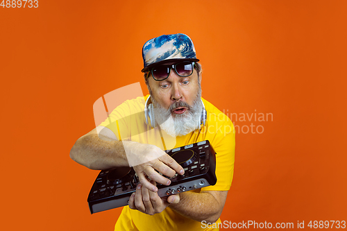 Image of Senior hipster man using devices, gadgets on orange background. Tech and joyful elderly lifestyle concept