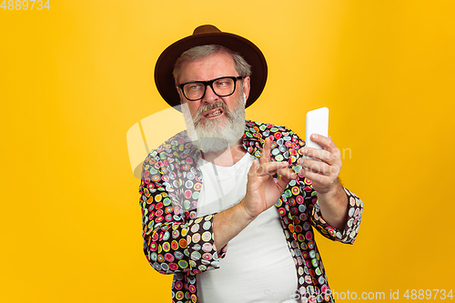 Image of Senior hipster man wearing eyeglasses posing on yellow background. Tech and joyful elderly lifestyle concept