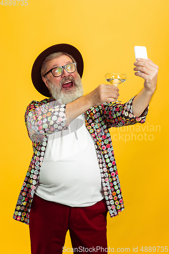 Image of Senior hipster man wearing eyeglasses posing on yellow background. Tech and joyful elderly lifestyle concept