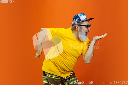 Image of Senior hipster man using devices, gadgets on orange background. Tech and joyful elderly lifestyle concept