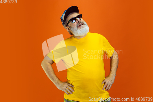 Image of Senior hipster man wearing eyeglasses posing on orange background. Tech and joyful elderly lifestyle concept