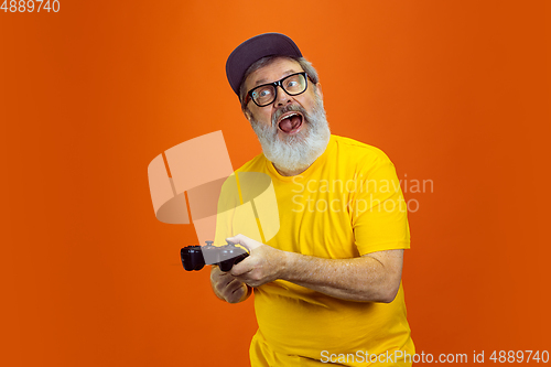 Image of Senior hipster man using devices, gadgets on orange background. Tech and joyful elderly lifestyle concept