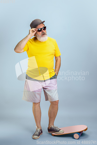 Image of Senior hipster man wearing eyeglasses posing on light blue background. Tech and joyful elderly lifestyle concept