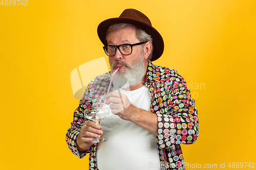 Image of Senior hipster man wearing eyeglasses posing on yellow background. Tech and joyful elderly lifestyle concept