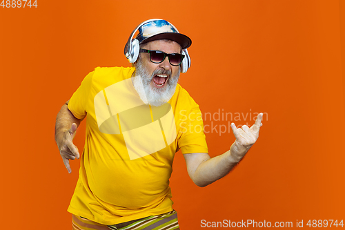 Image of Senior hipster man using devices, gadgets on orange background. Tech and joyful elderly lifestyle concept