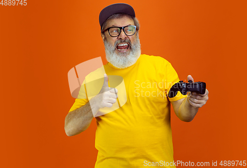 Image of Senior hipster man using devices, gadgets on orange background. Tech and joyful elderly lifestyle concept