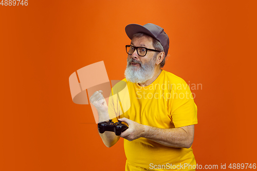 Image of Senior hipster man using devices, gadgets on orange background. Tech and joyful elderly lifestyle concept