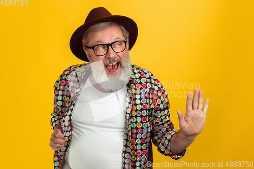 Image of Senior hipster man wearing eyeglasses posing on yellow background. Tech and joyful elderly lifestyle concept