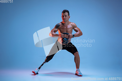 Image of Athlete with disabilities or amputee isolated on blue studio background. Professional male sportsman with leg prosthesis training with weights in neon