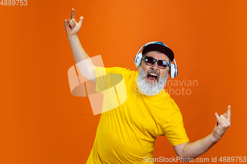 Image of Senior hipster man using devices, gadgets on orange background. Tech and joyful elderly lifestyle concept