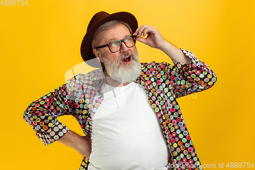 Image of Senior hipster man wearing eyeglasses posing on yellow background. Tech and joyful elderly lifestyle concept