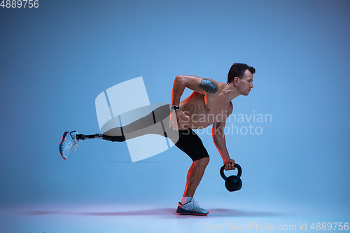 Image of Athlete with disabilities or amputee isolated on blue studio background. Professional male sportsman with leg prosthesis training with weights in neon