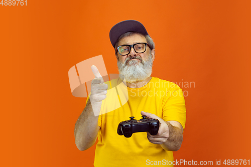 Image of Senior hipster man using devices, gadgets on orange background. Tech and joyful elderly lifestyle concept