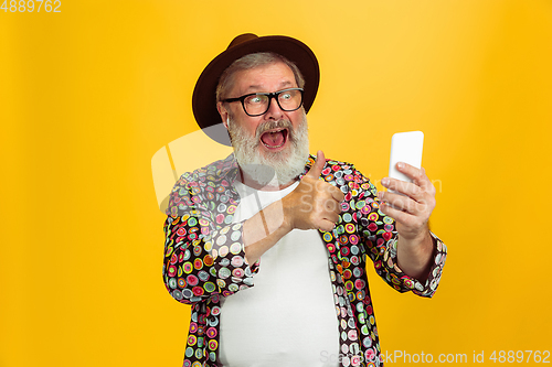 Image of Senior hipster man wearing eyeglasses posing on yellow background. Tech and joyful elderly lifestyle concept