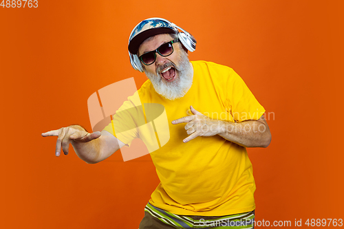 Image of Senior hipster man using devices, gadgets on orange background. Tech and joyful elderly lifestyle concept