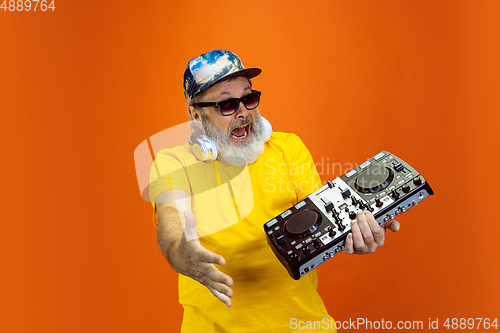 Image of Senior hipster man using devices, gadgets on orange background. Tech and joyful elderly lifestyle concept