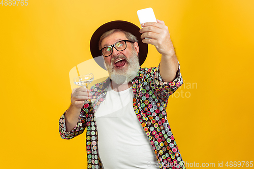 Image of Senior hipster man wearing eyeglasses posing on yellow background. Tech and joyful elderly lifestyle concept