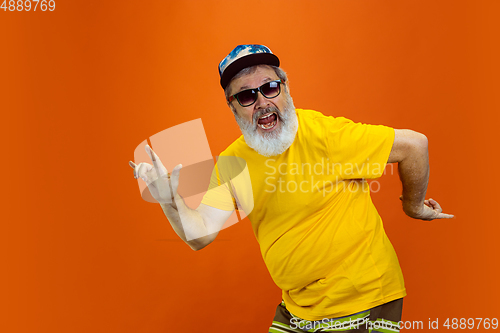 Image of Senior hipster man using devices, gadgets on orange background. Tech and joyful elderly lifestyle concept