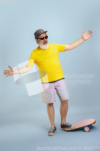 Image of Senior hipster man wearing eyeglasses posing on light blue background. Tech and joyful elderly lifestyle concept