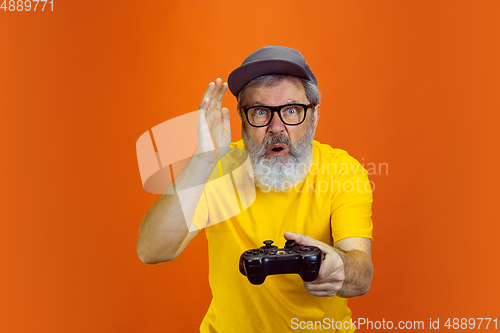 Image of Senior hipster man using devices, gadgets on orange background. Tech and joyful elderly lifestyle concept