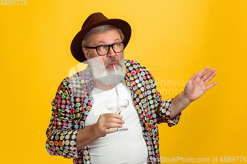 Image of Senior hipster man wearing eyeglasses posing on yellow background. Tech and joyful elderly lifestyle concept