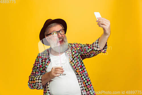 Image of Senior hipster man wearing eyeglasses posing on yellow background. Tech and joyful elderly lifestyle concept