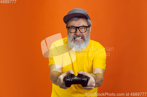 Image of Senior hipster man using devices, gadgets on orange background. Tech and joyful elderly lifestyle concept